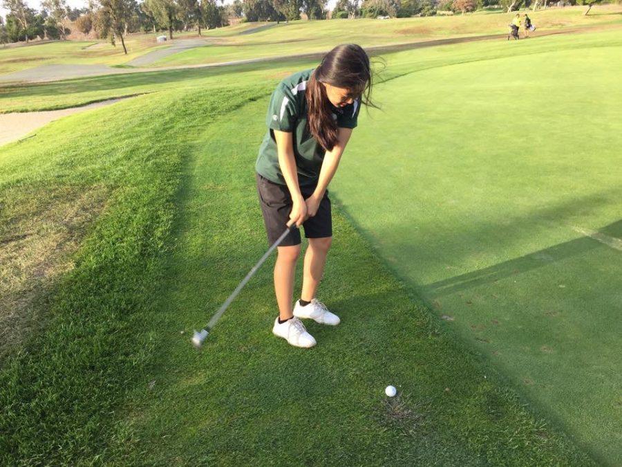Junior Joyce Choi swings back her club to chip the golf ball onto the putting green.